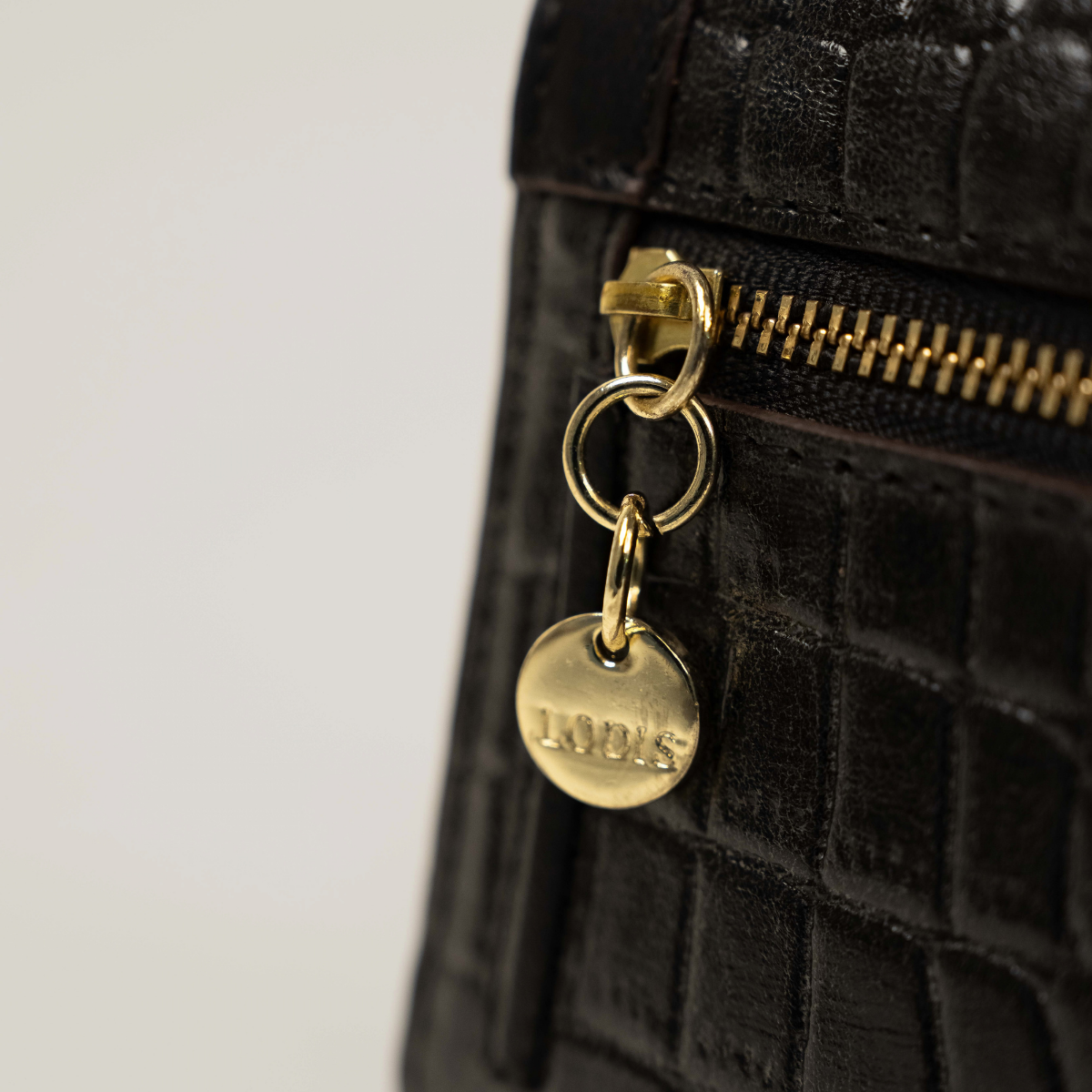 Lodis Amara Checkbook Clutch in Black - Close-Up of Gold-Tone Zipper Pull with Engraved Lodis Coin Charm on Black Croco-Embossed Leather | Lodis 1965