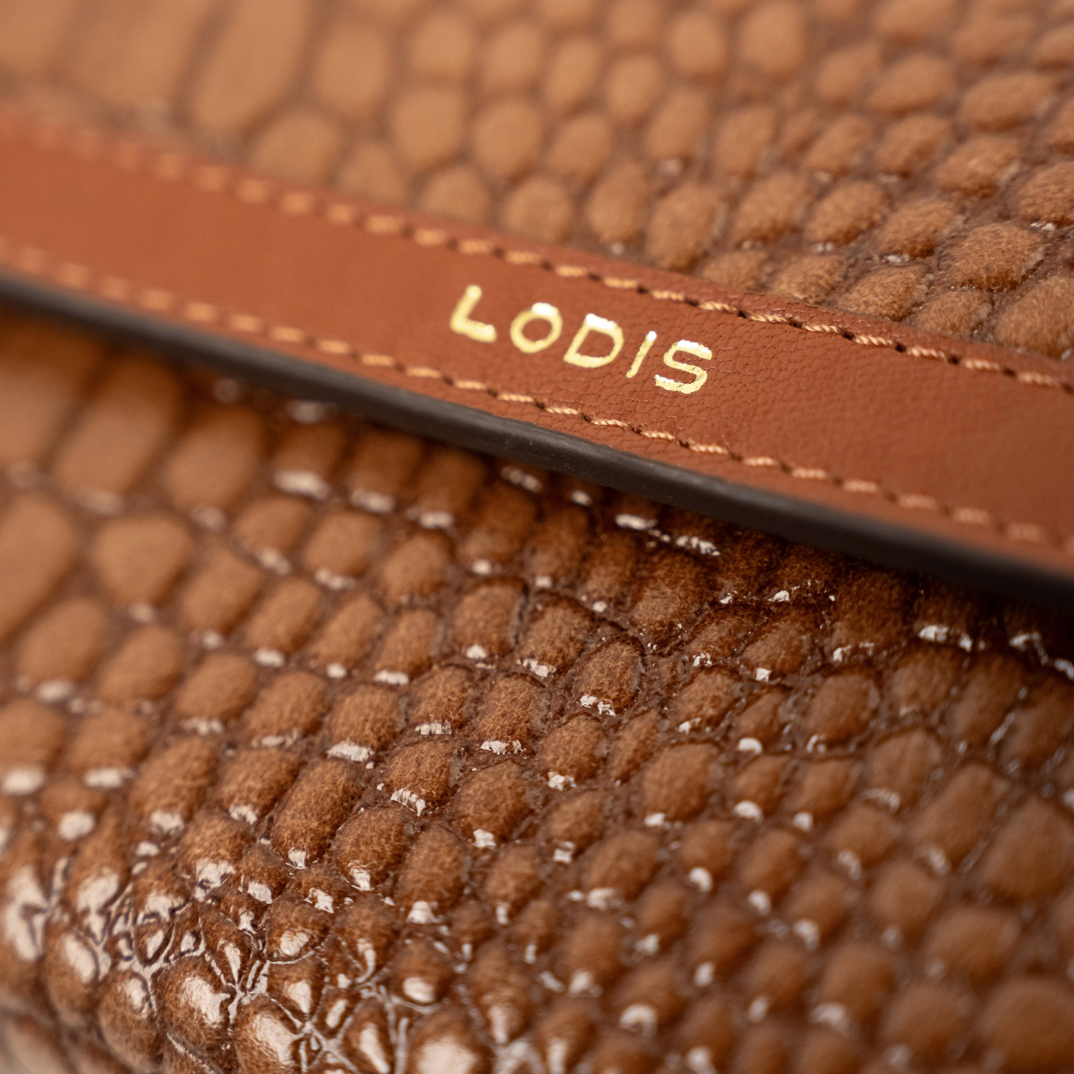 Lodis Amara Checkbook Clutch in Chestnut - Close-Up of Gold Foil Lodis Logo on Stitched Texas Leather Band Across Glossy Croco-Embossed Flap | Lodis 1965