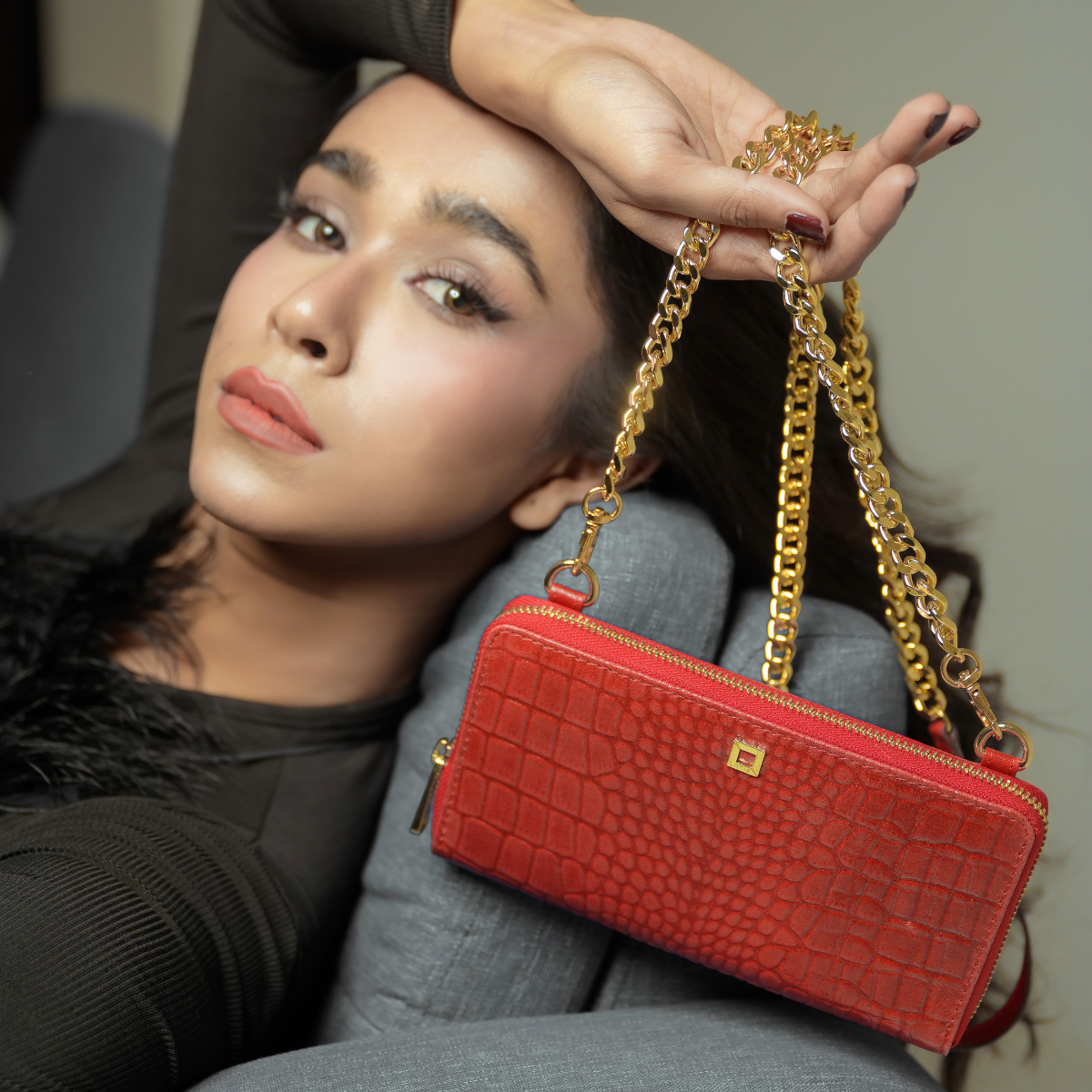 Woman Posing with Lodis Amara Sling in Samba Held by Gold-Tone Chain Strap - Fall Lifestyle Shot with Black Top in Studio Setting, Glossy Croco-Embossed Leather | Lodis 1965