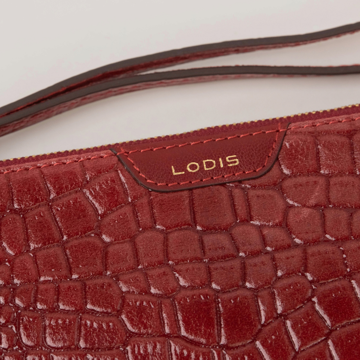 Lodis Amara Zip Pouch in Samba - Close-Up of Gold Foil Lodis Logo on Smooth Texas Leather Tab with Wristlet Strap Above Croco-Embossed Texture | Lodis 1965