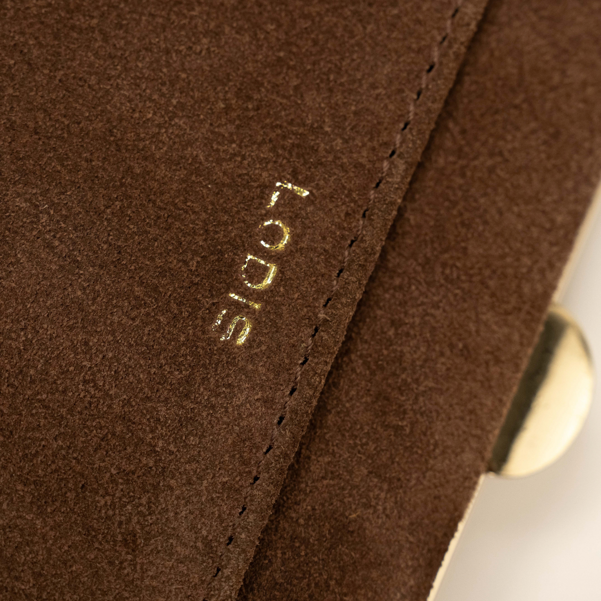Lodis Celara Frame Clutch in Brown - Close-Up of Gold Foil Lodis Logo and Stitched Pocket Edge on Chocolate Brown Texas Suede | Lodis 1965