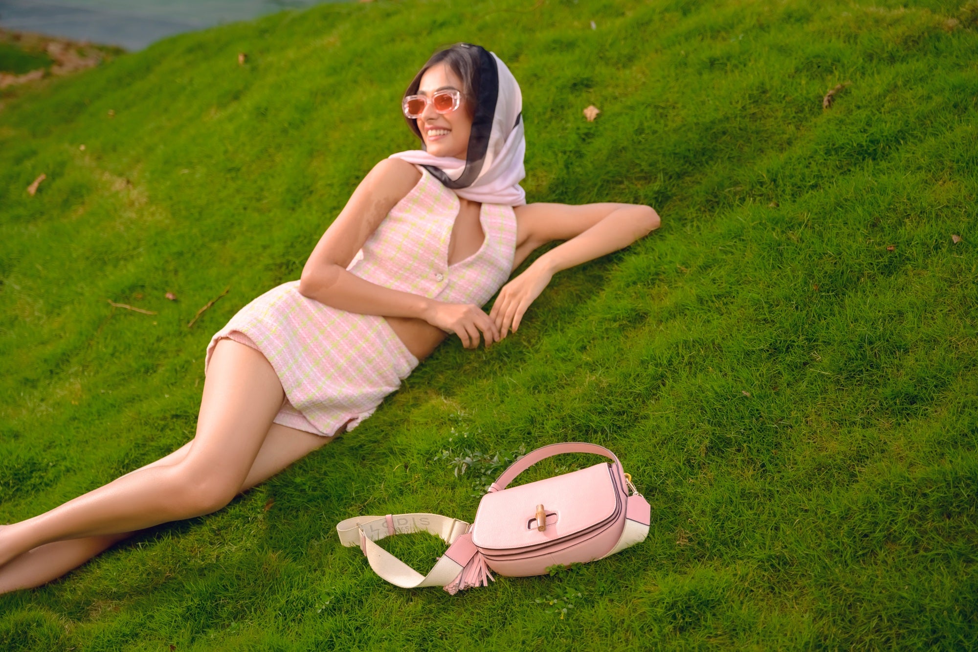 Woman Reclining on Grass with Lodis Sondra Top Handle Crossbody in Dusty Rose – Outdoor Lifestyle Shot Showing Bamboo Turn-Lock and Woven Strap | Lodis 1965