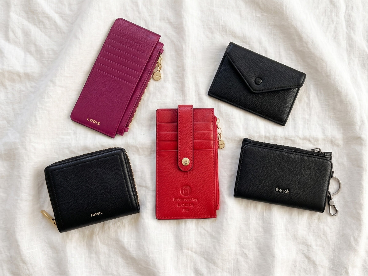 Five slim leather wallets flat lay - magenta long stacker, red card stacker, black zip wallet, black envelope card case, and black bifold with keyring on white linen | Lodis 1965