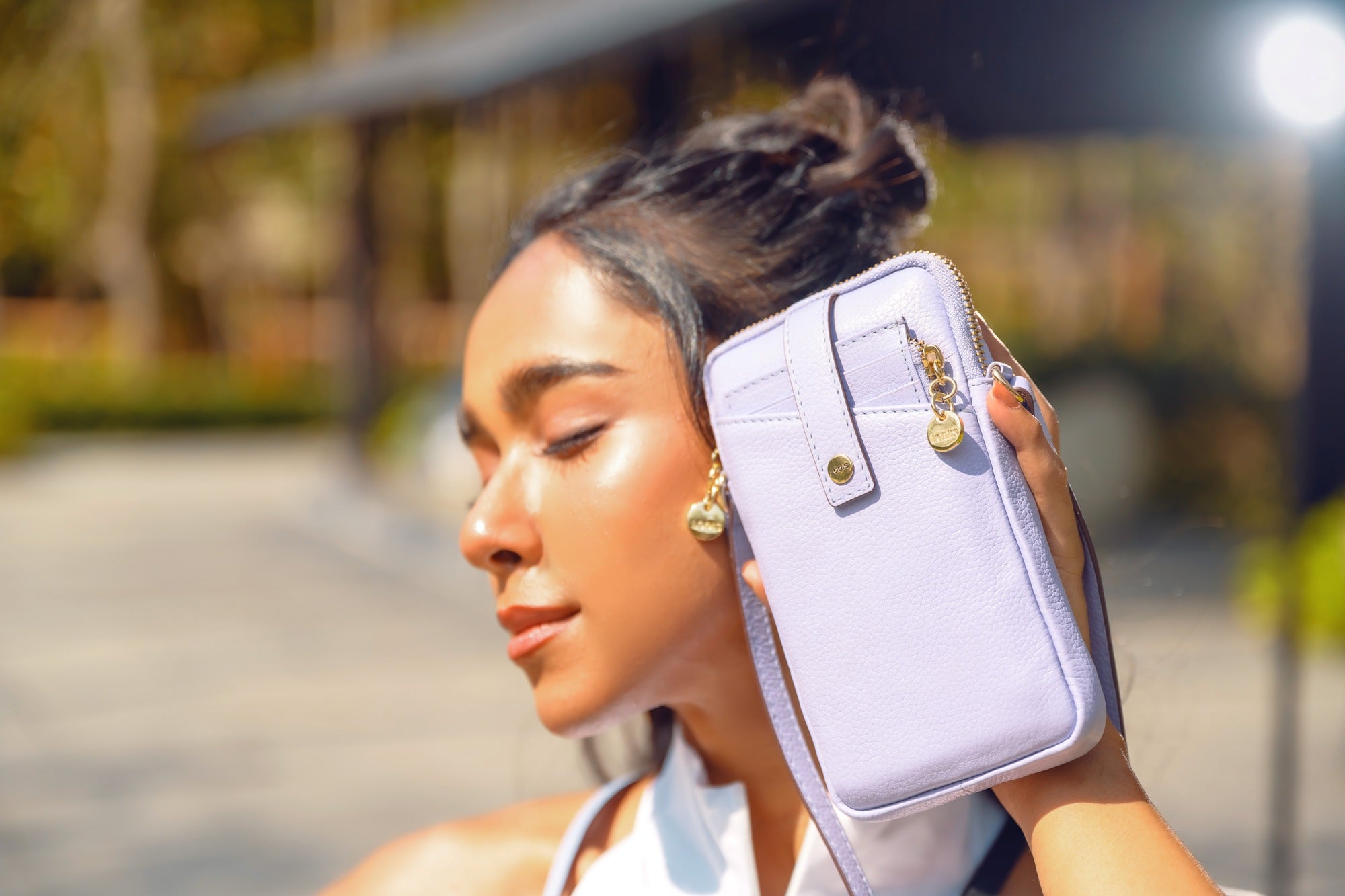 Lodis Catalina City Sling white leather crossbody phone bag held by a woman in an outdoor lifestyle shot with gold hardware detail