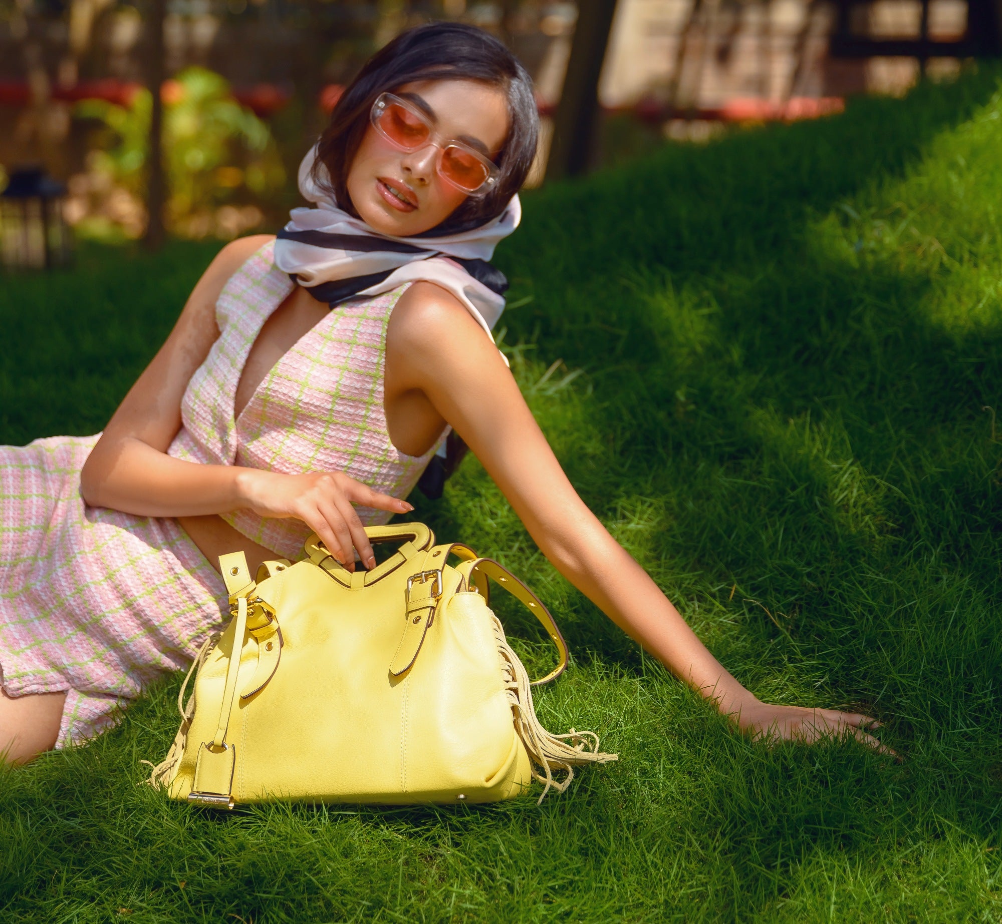 Lodis Skya Tote yellow leather fringe handbag worn by a woman sitting on grass in a summer outdoor setting