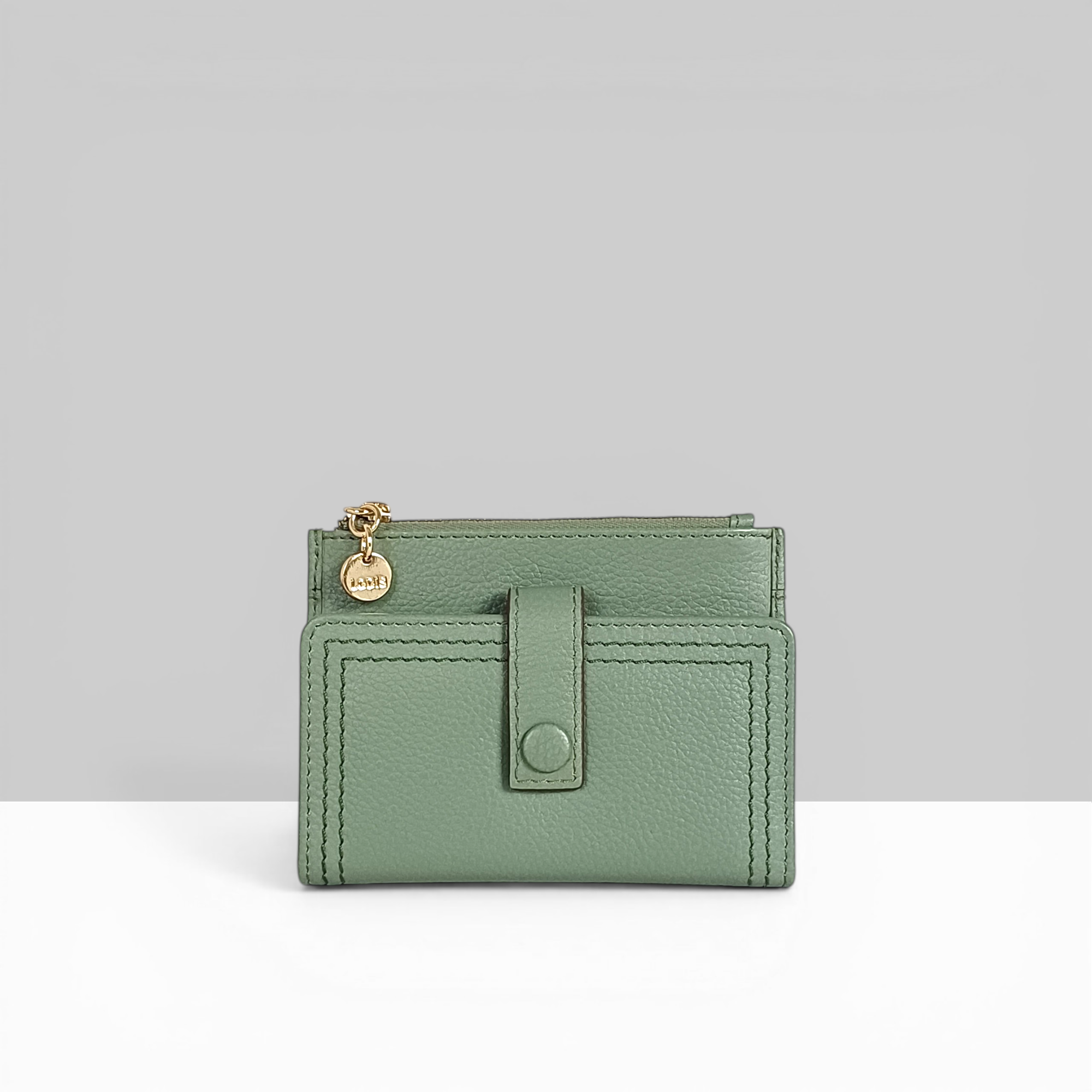 Lodis Kiara Flip Face Wallet in sage green pebbled leather with snap closure, tab strap, and gold Lodis charm – front view