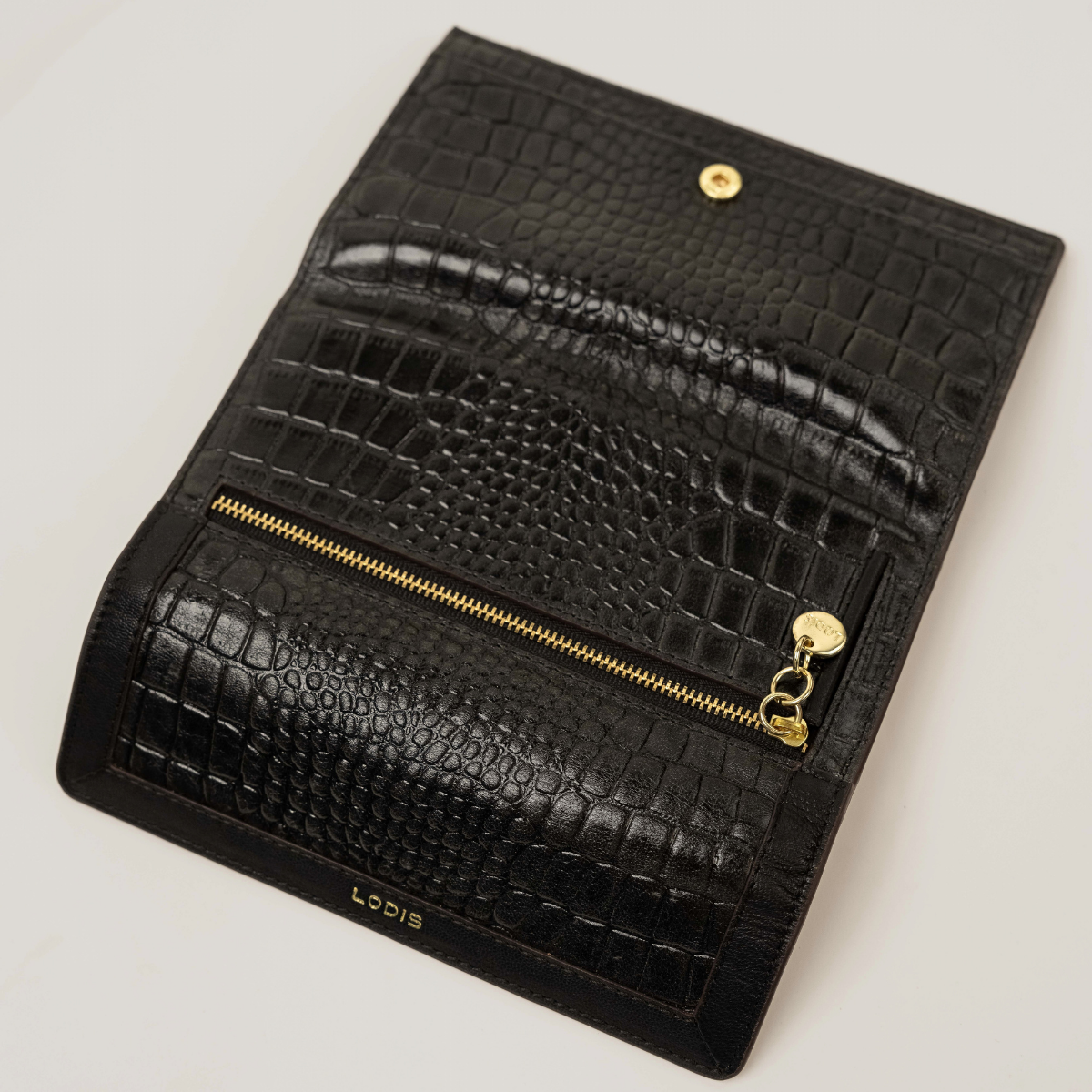 Lodis Amara Checkbook Clutch in Black - Overhead Angled View Showing Snap Flap Closure, Back Zip Pocket and Glossy Croco-Embossed Texture | Lodis 1965
