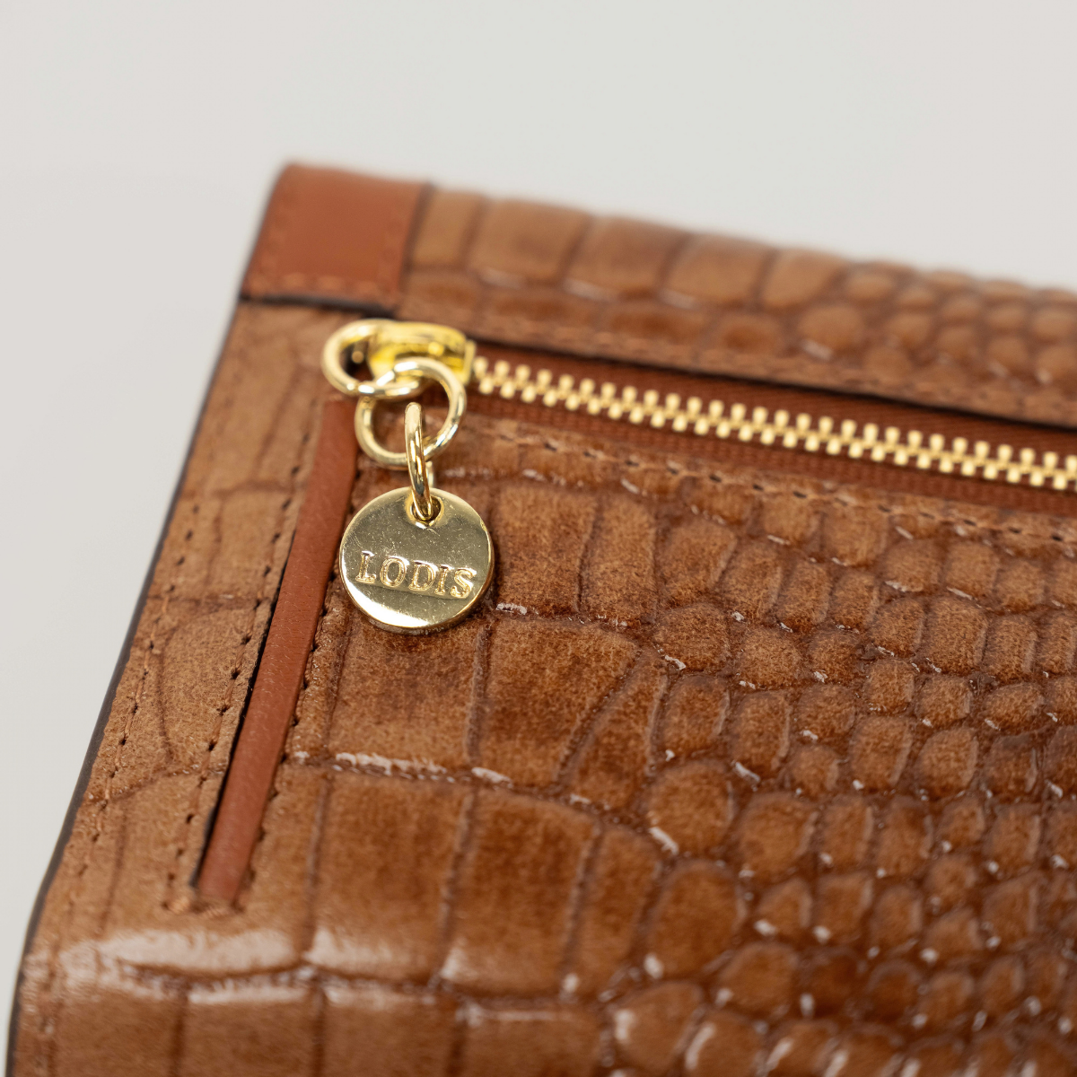 Lodis Amara Checkbook Clutch in Chestnut - Close-Up of Gold-Tone Zipper Pull with Engraved Lodis Coin Charm on Back Zip Pocket | Lodis 1965