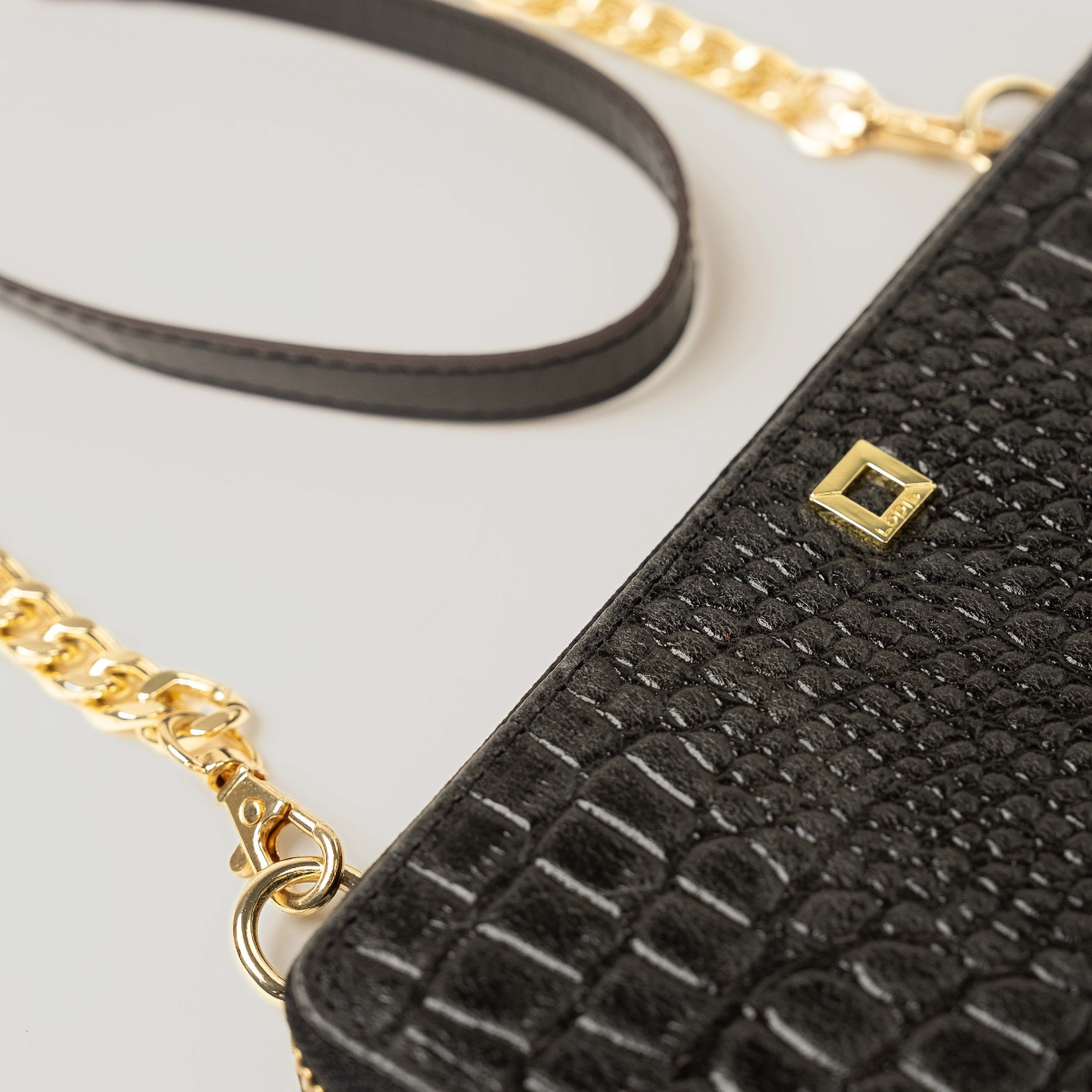 Lodis Amara Sling in Black - Angled Detail of Gold-Tone Chain, Smooth Leather Shoulder Strap and Square Logo Plate on Black Croco-Embossed Leather | Lodis 1965
