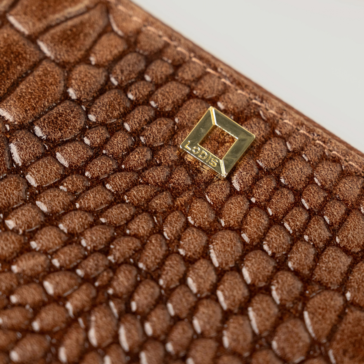 Lodis Amara Sling in Chestnut - Close-Up of Gold-Tone Square Logo Plate on Cognac Brown Glossy Croco-Embossed Leather | Lodis 1965