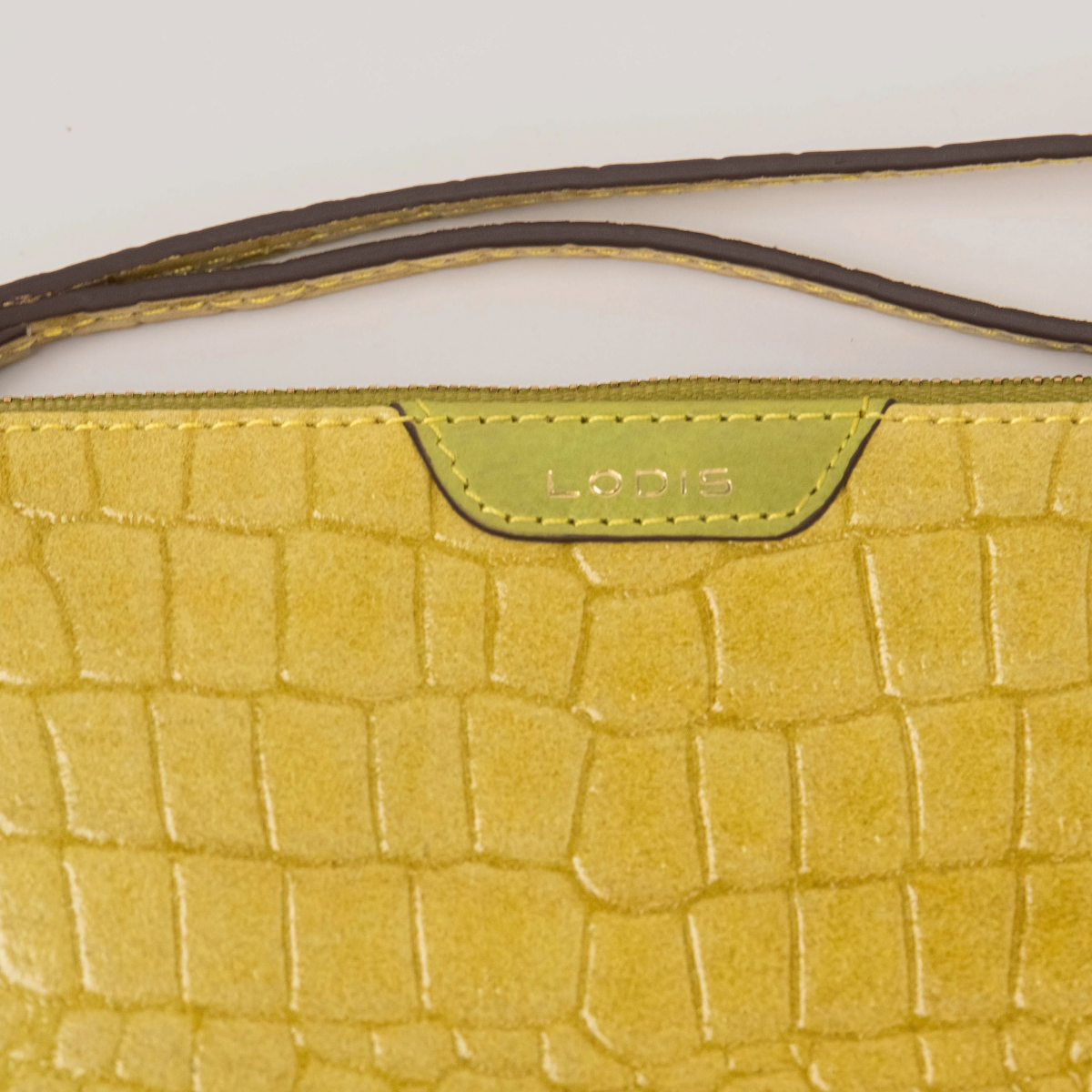 Lodis Amara Zip Pouch in Curry - Close-Up of Gold Foil Lodis Logo on Smooth Texas Leather Tab with Wristlet Strap Above Croco-Embossed Texture | Lodis 1965