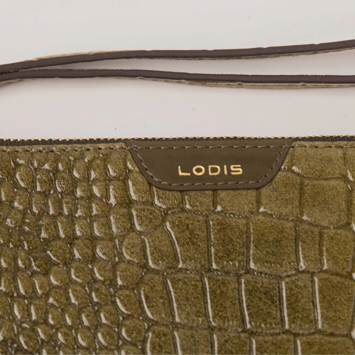 Lodis Amara Zip Pouch in Olivine - Close-Up of Gold Foil Lodis Logo on Smooth Texas Leather Tab with Wristlet Strap Above Croco-Embossed Texture | Lodis 1965