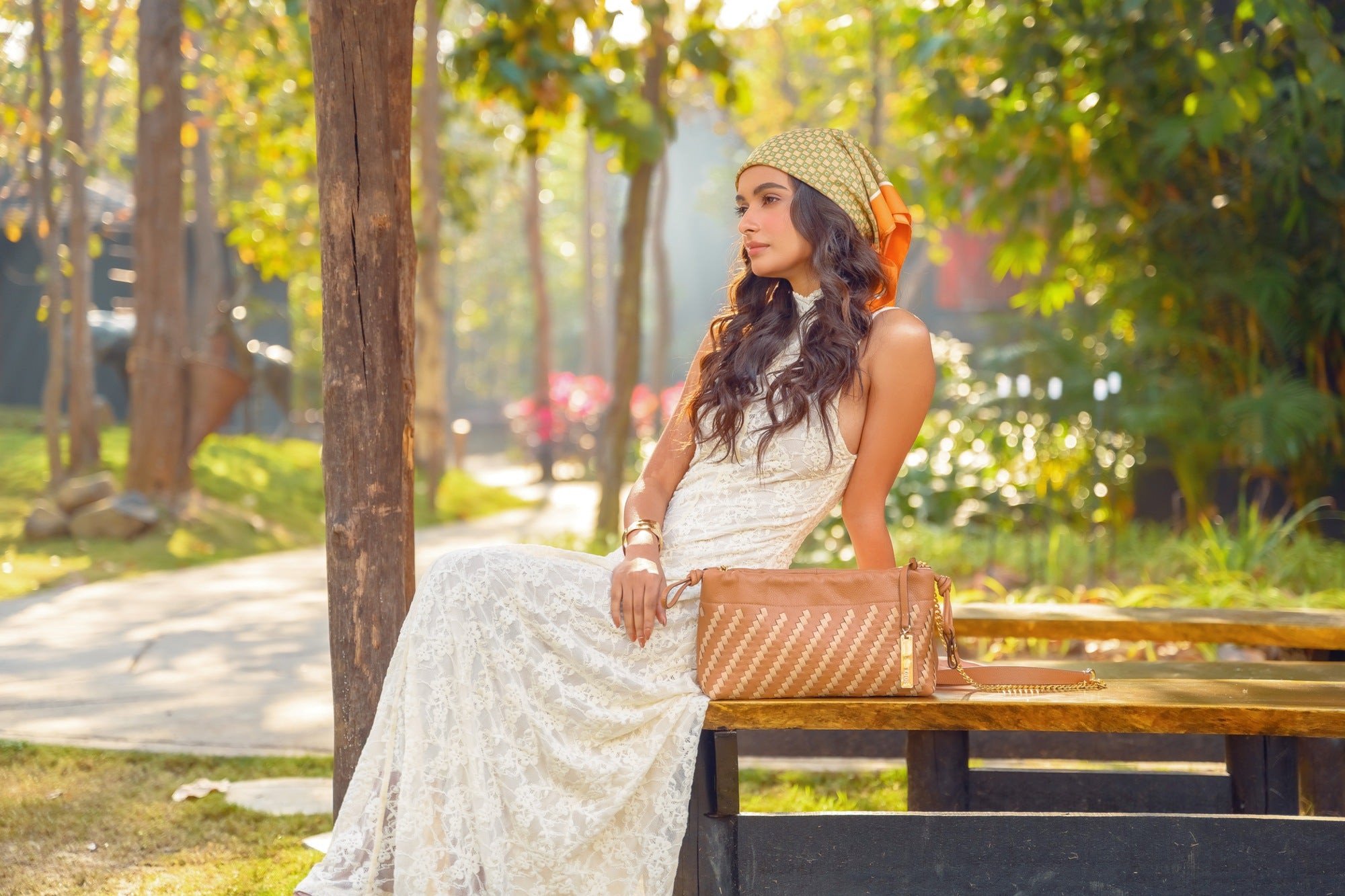 Woman in White Lace Dress Seated Outdoors with Lodis Solstice Pouch in Chestnut – Lifestyle Shot Showing Two-Tone Woven Leather and Gold-Tone Chain Strap | Lodis 1965