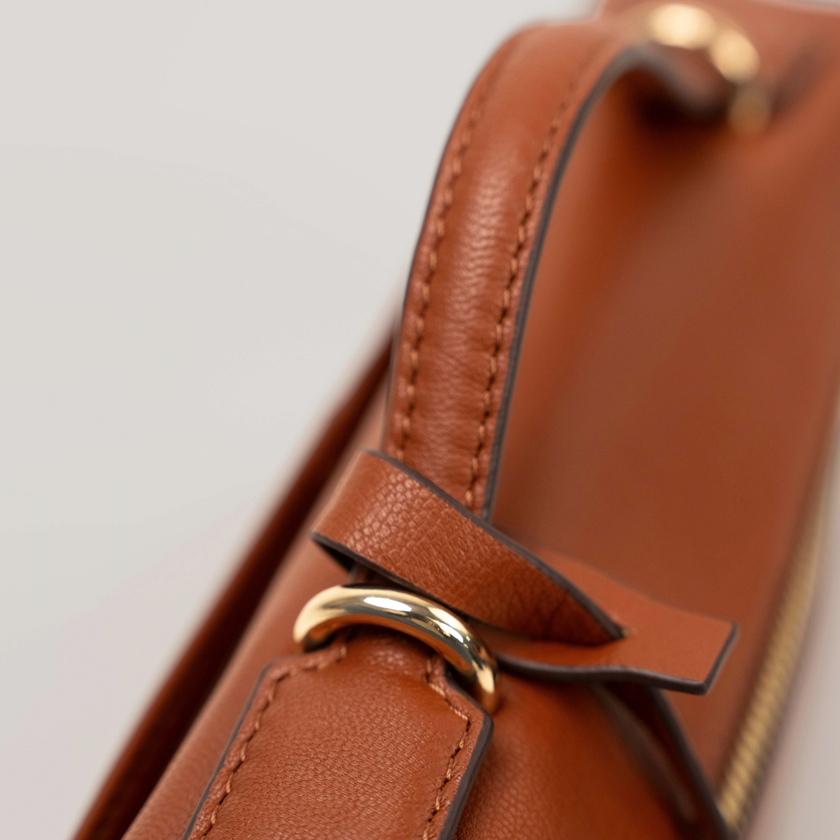Lodis Stratos Texas Crossbody in Rust - Detail of Knotted Texas Leather Handle Tie and Gold-Tone Ring Against Rust Leather Body | Lodis 1965