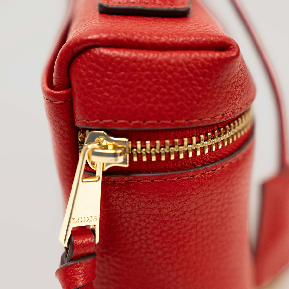 Lodis Stratos Texas Crossbody in Samba - Close-Up of Engraved Gold-Tone Lodis Zipper Pull on Deep Red Texas Leather Corner | Lodis 1965